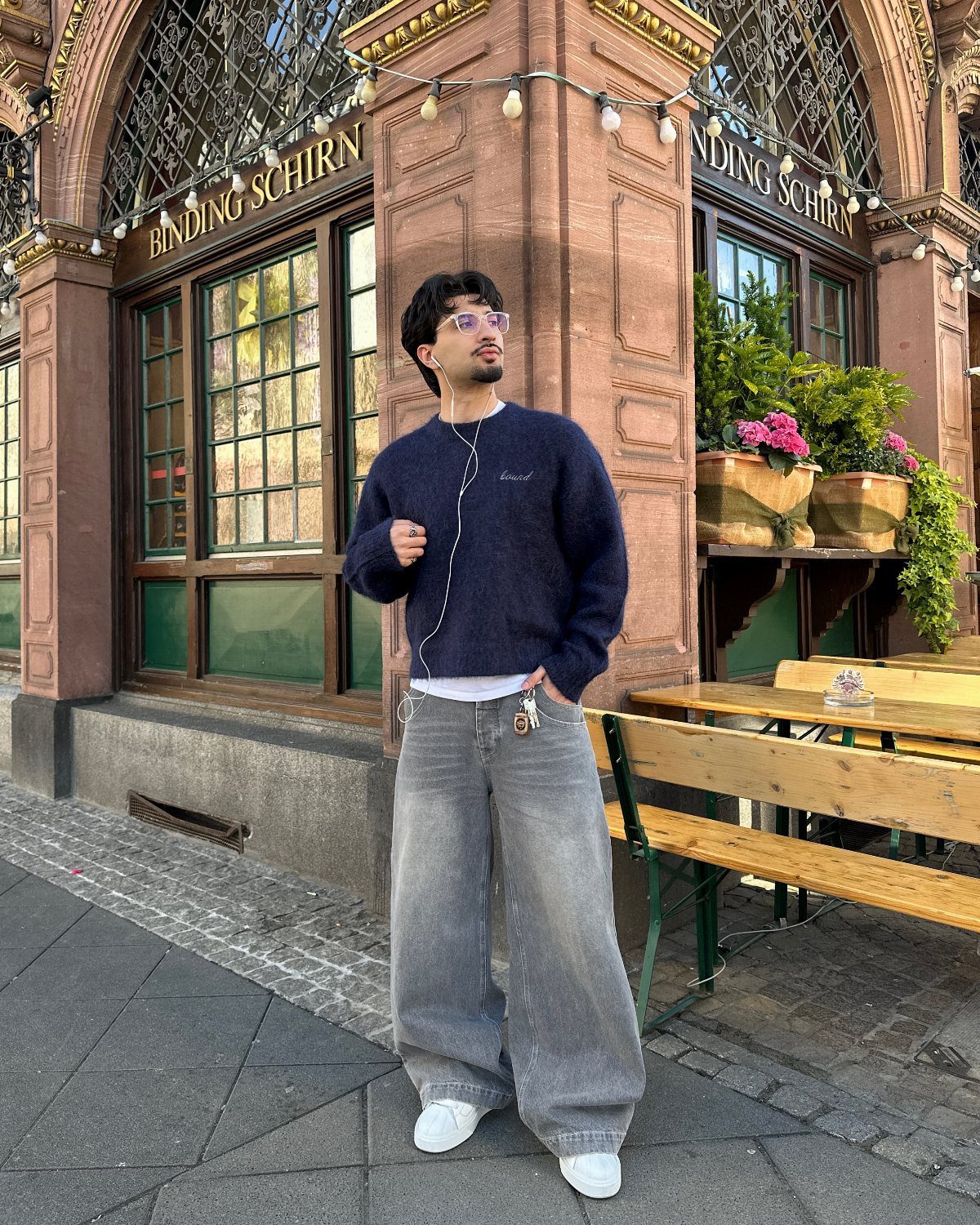 Man wearing a dark blue crew-neck sweater and wide-leg blue jeans with white sneakers.