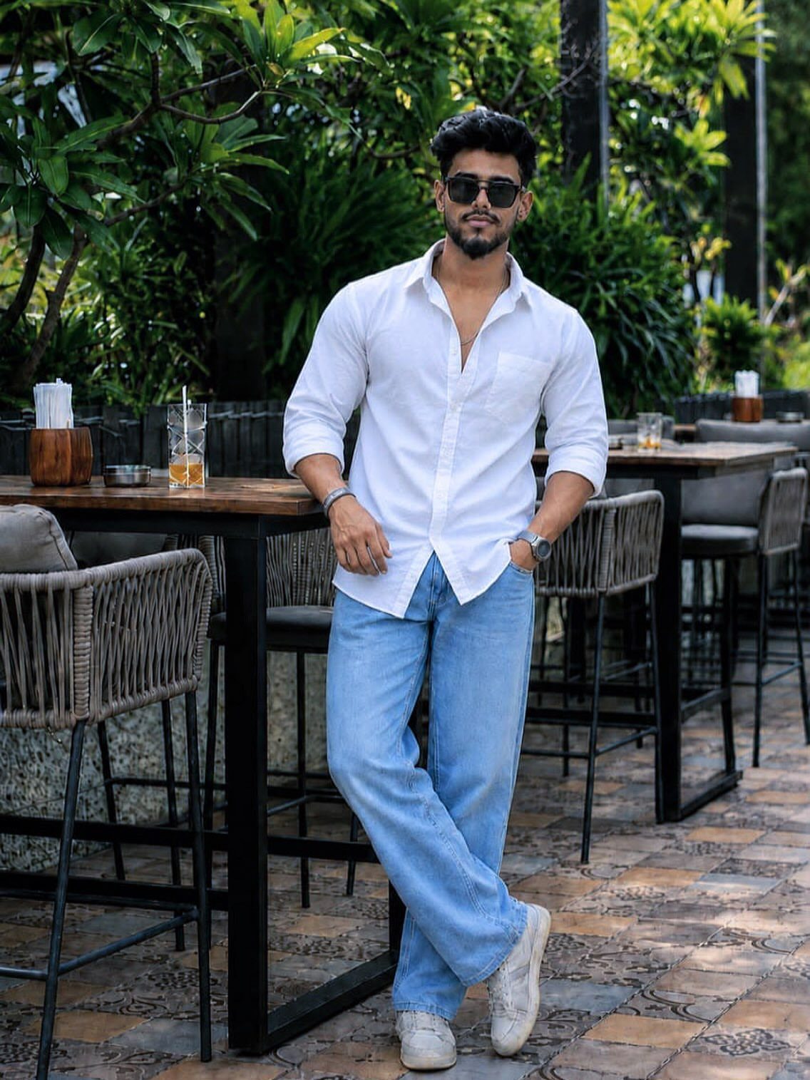 Man wearing a white button-down shirt and light blue jeans standing at a cafe.