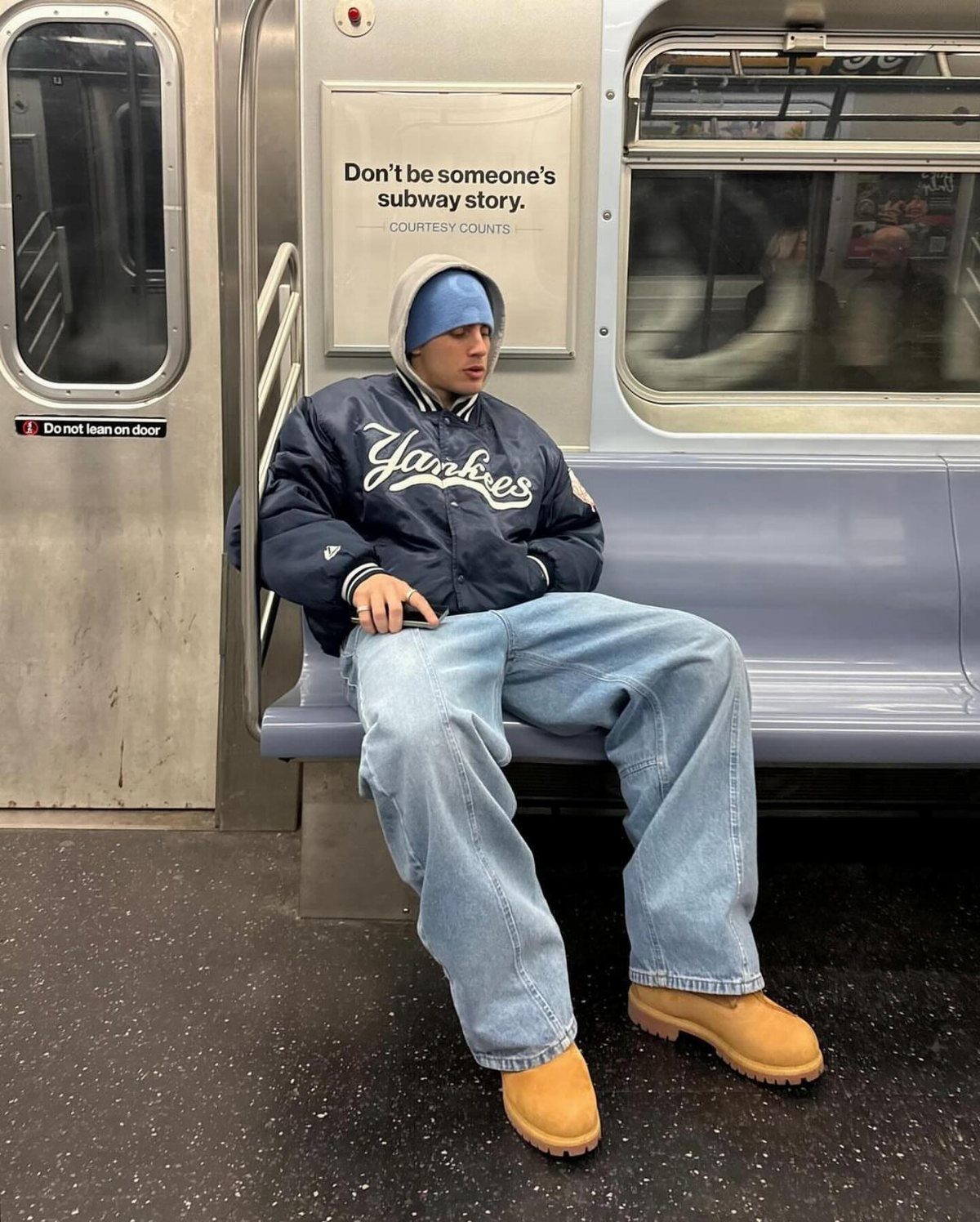 Man in a subway wearing light blue jeans and tan winter boots.