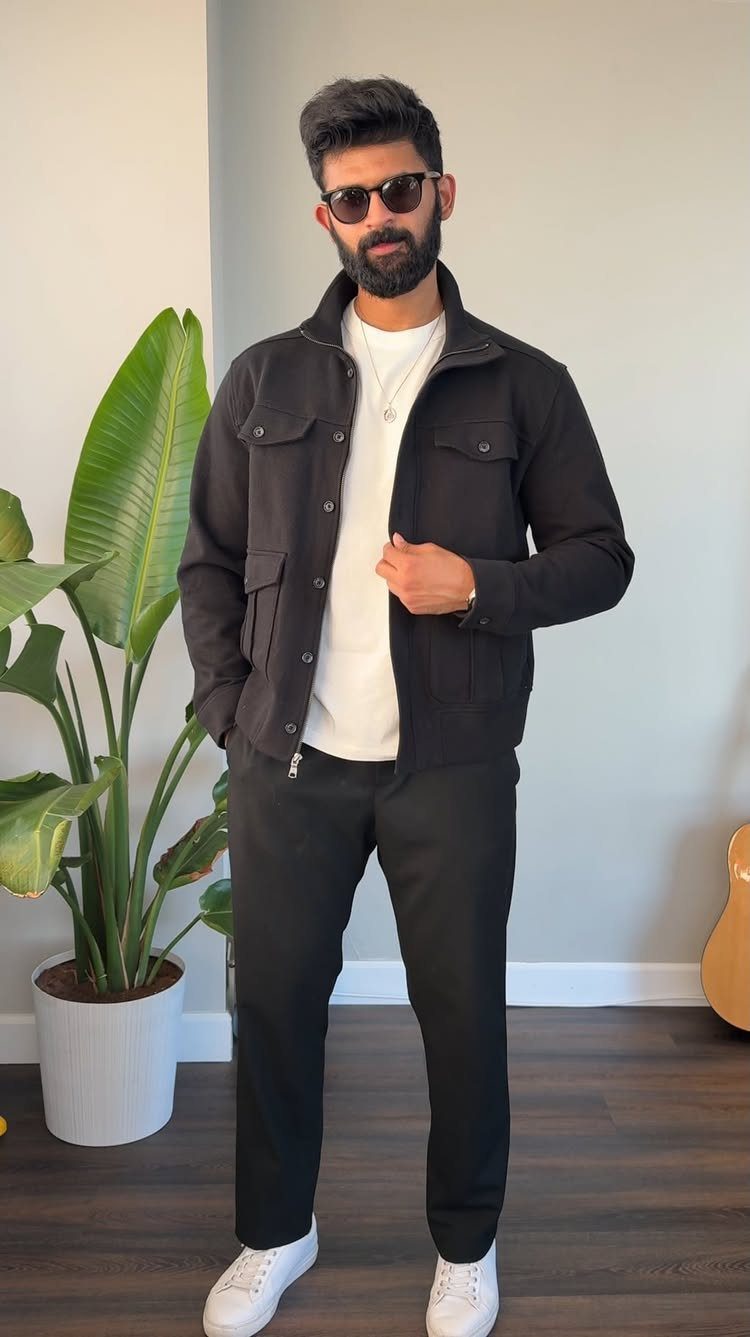 Man wearing a black jacket over a white t-shirt and black trousers.