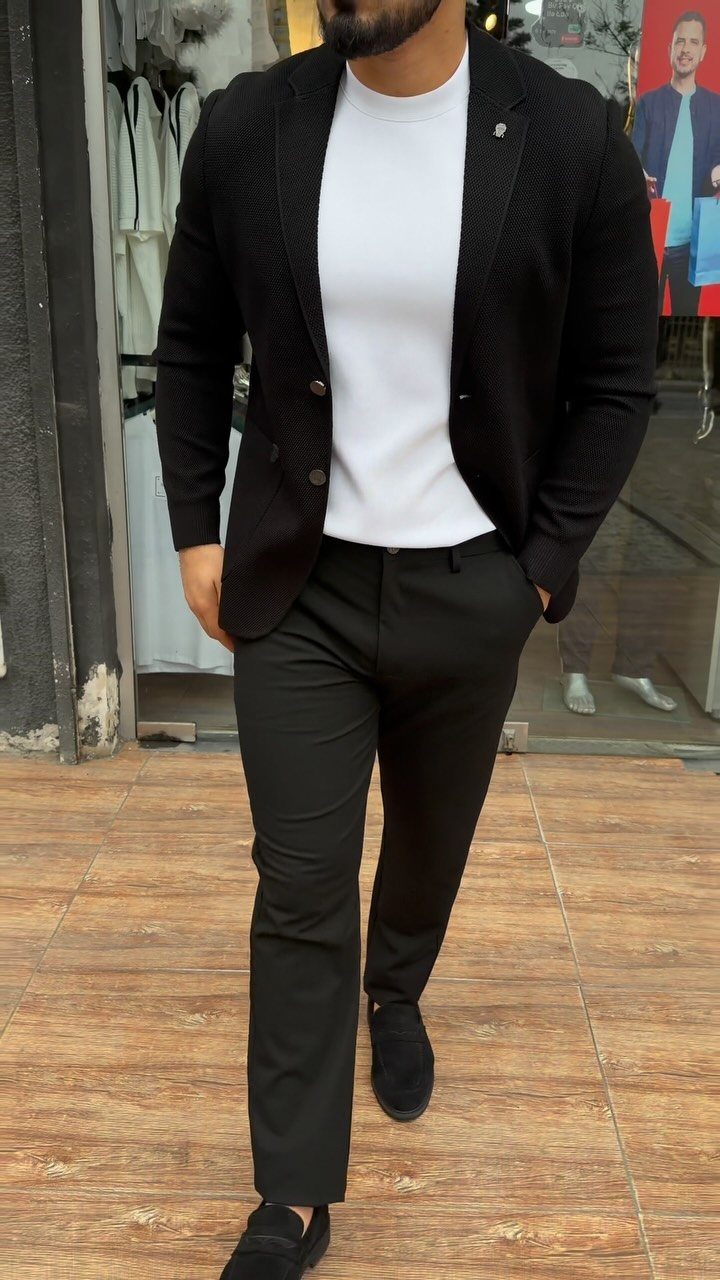 Man wearing a black blazer, white t-shirt, and black trousers on wooden flooring.