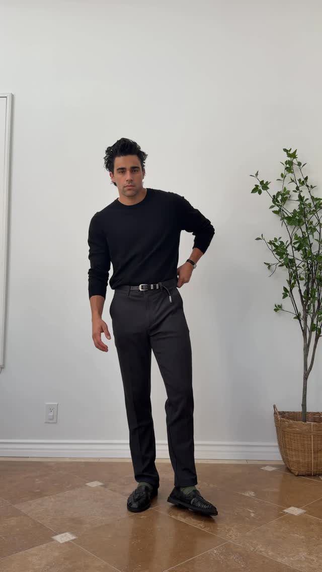 Man wearing a black long-sleeved shirt and dark grey chinos with black loafers.