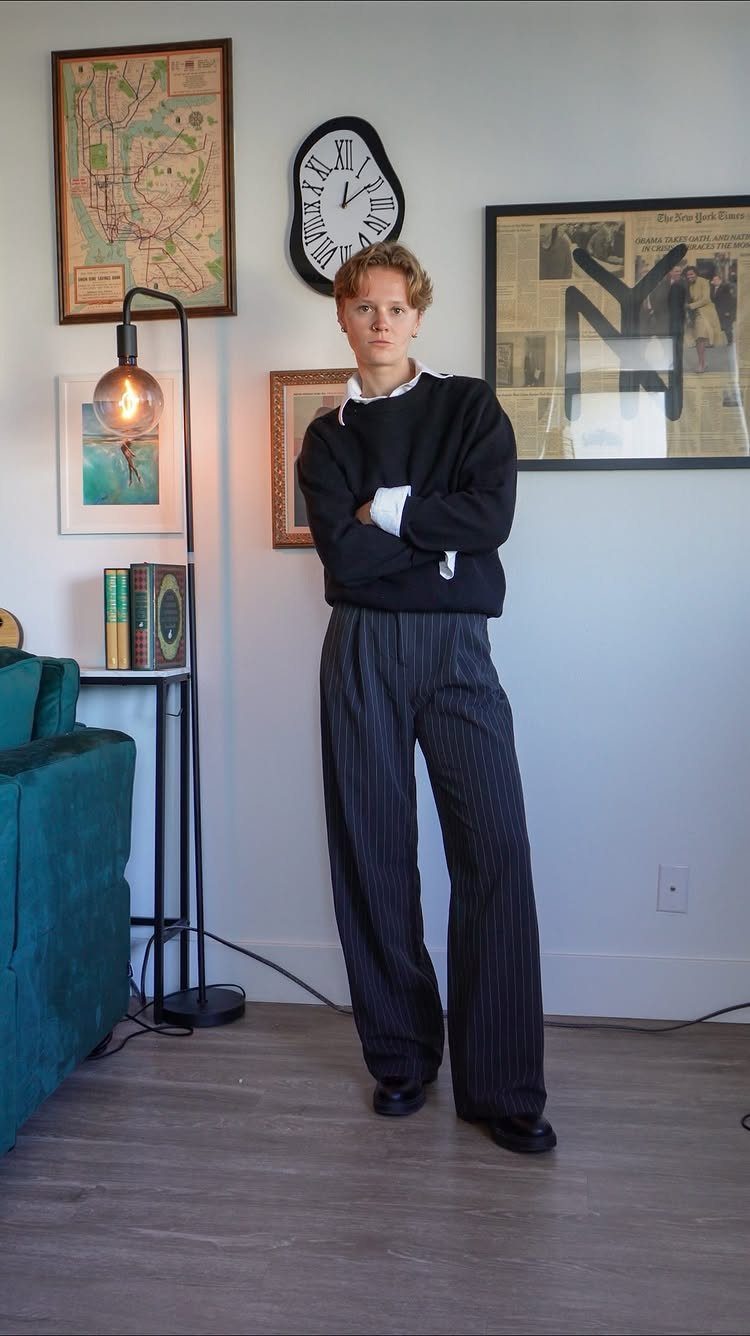 Man wearing a black sweater over a white shirt and pinstriped trousers.