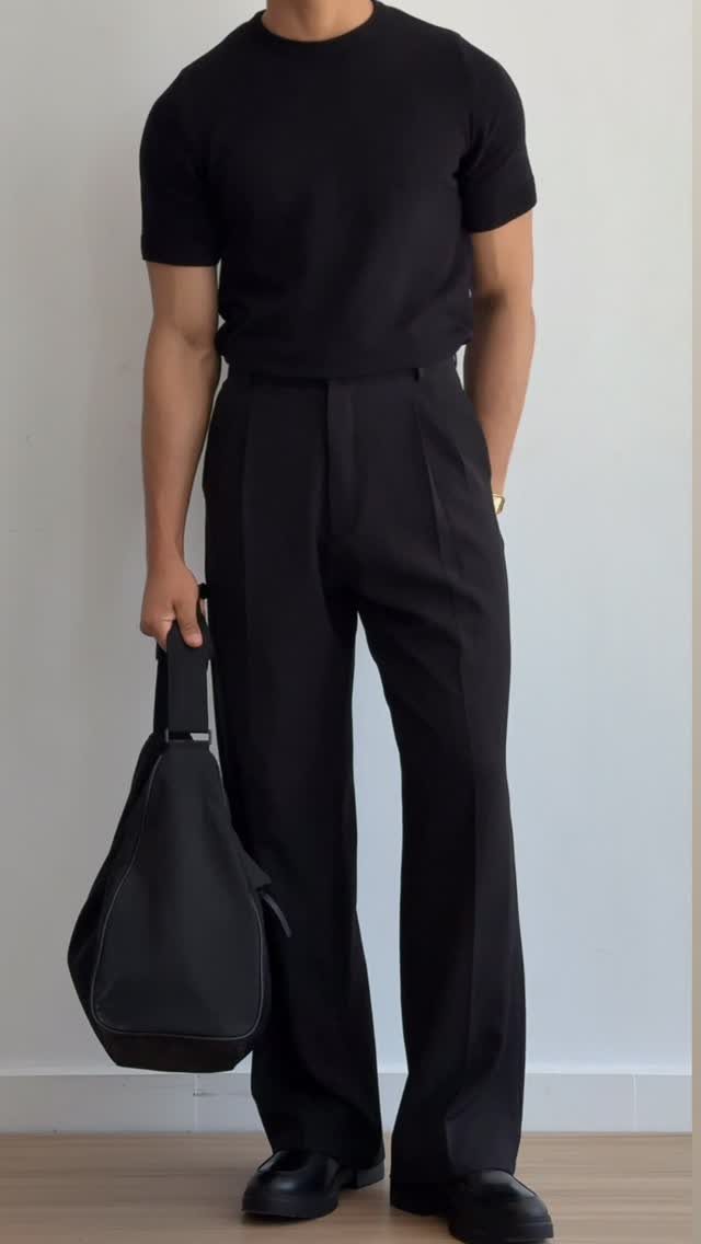 Man wearing an all-black outfit with a t-shirt, trousers, and leather bag.