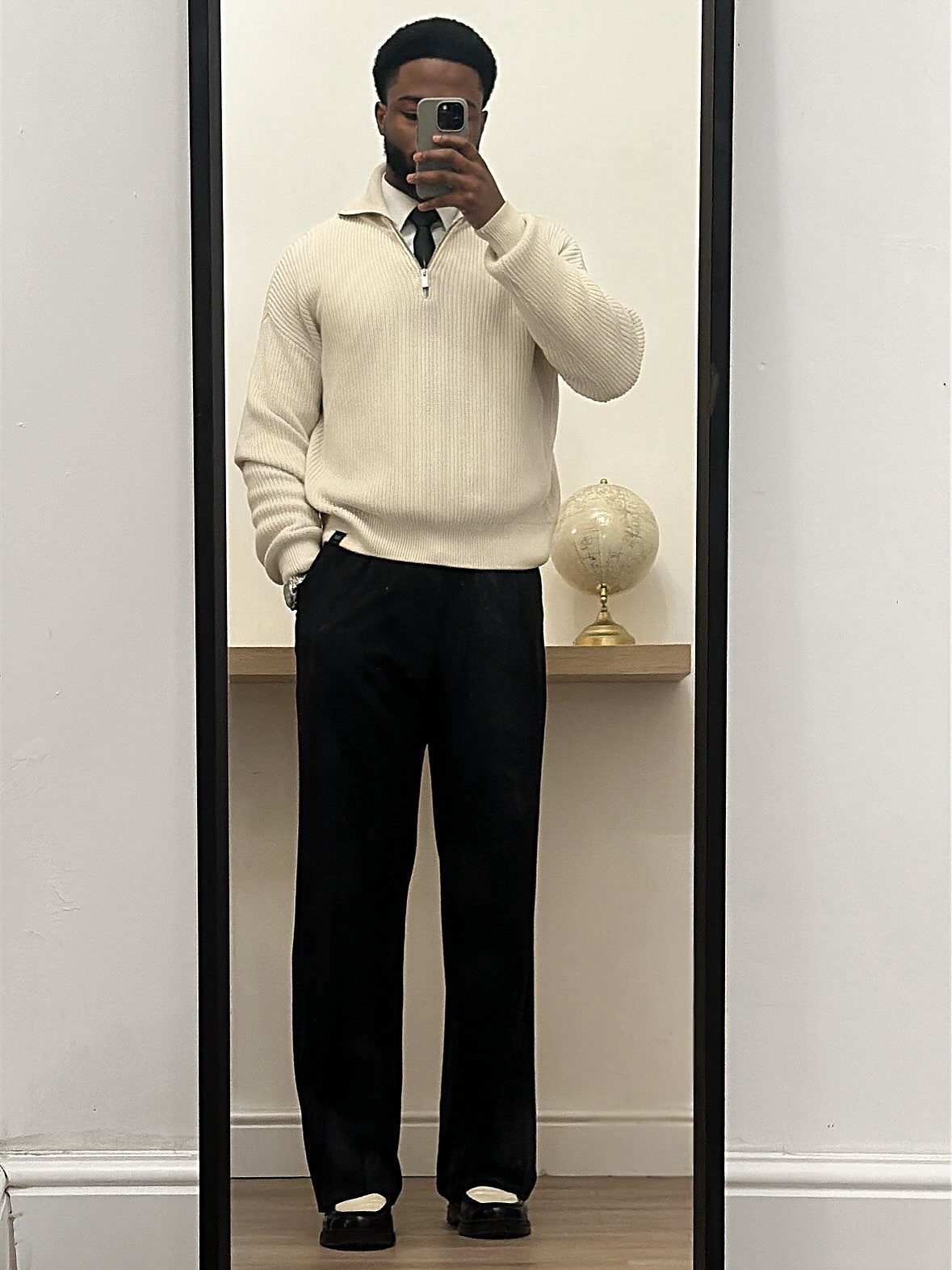 Man in cream quarter-zip sweater, white shirt, tie, and black wide-leg trousers.