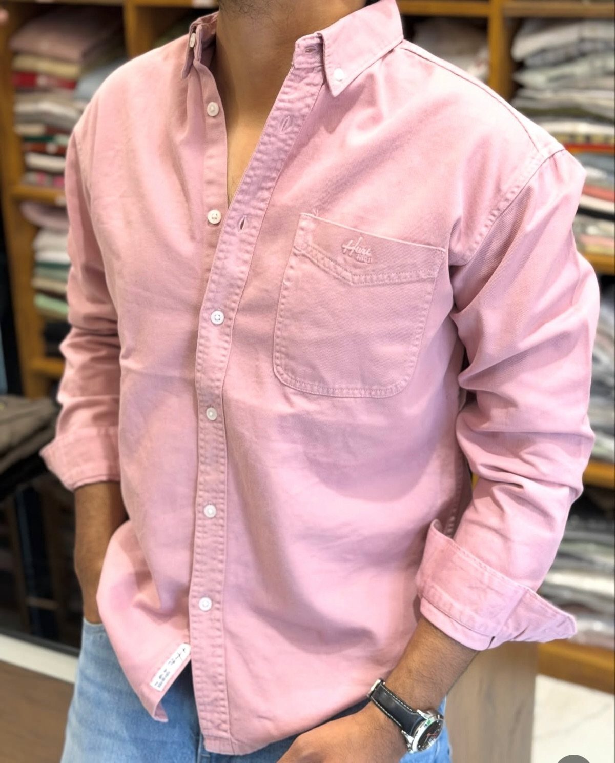 Man wearing a pink button-down shirt and light blue jeans in a store