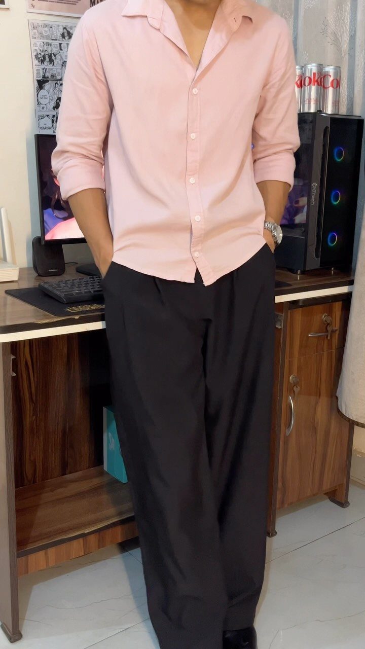 Man wearing a pink button-down shirt and black trousers standing by a desk.