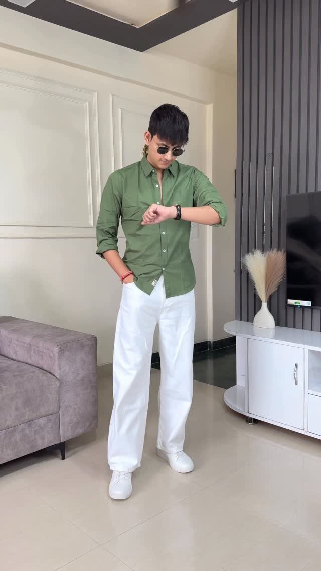 Man wearing olive green shirt and wide white trousers in a modern room