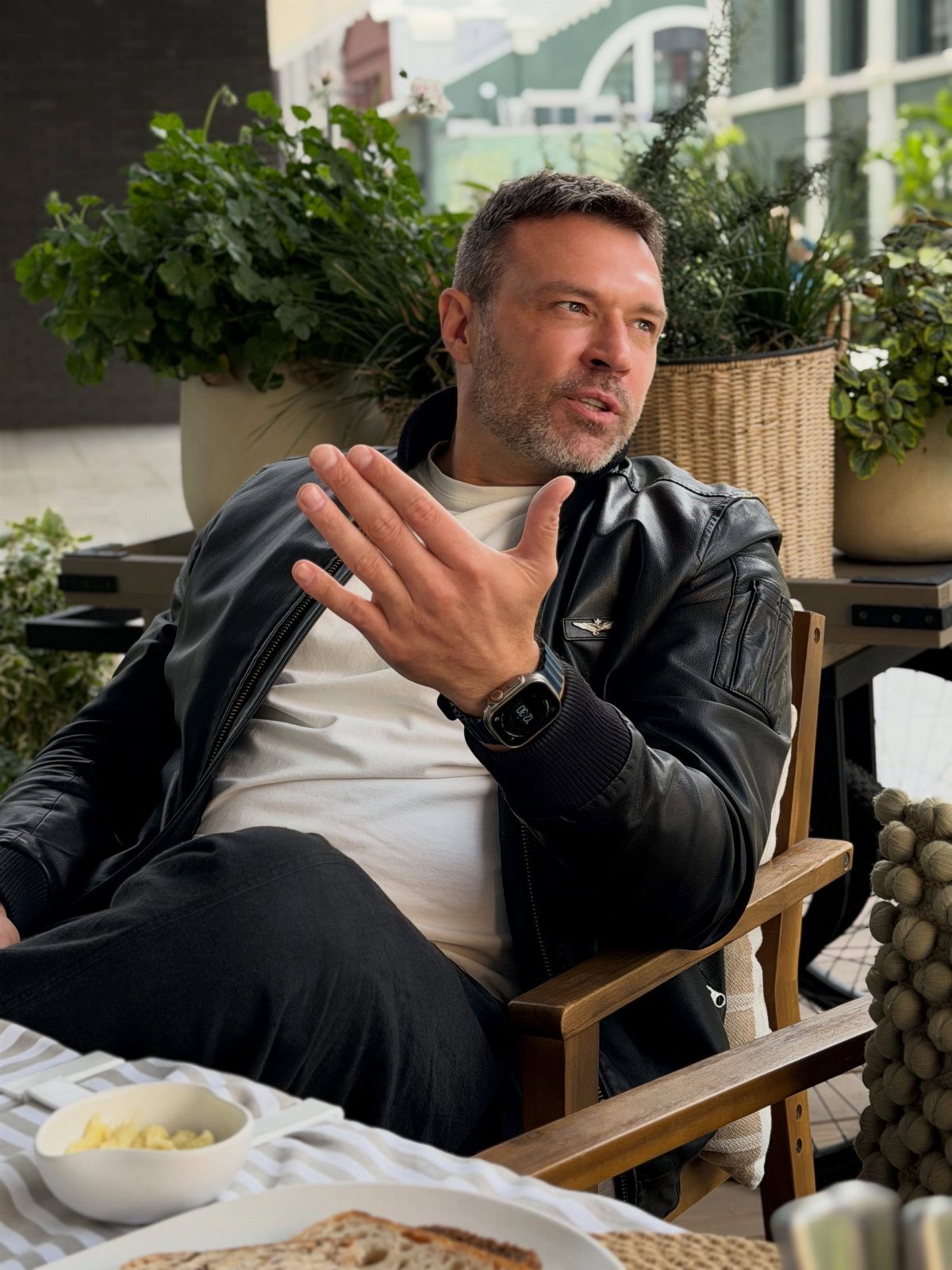 Man wearing a black leather jacket and white t-shirt sitting outdoors.