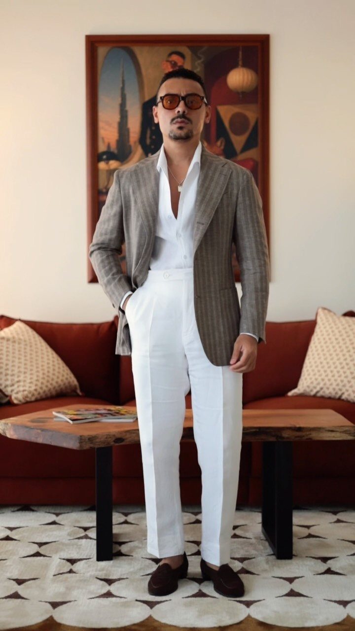 Man wearing a brown blazer and white trousers standing in a living room