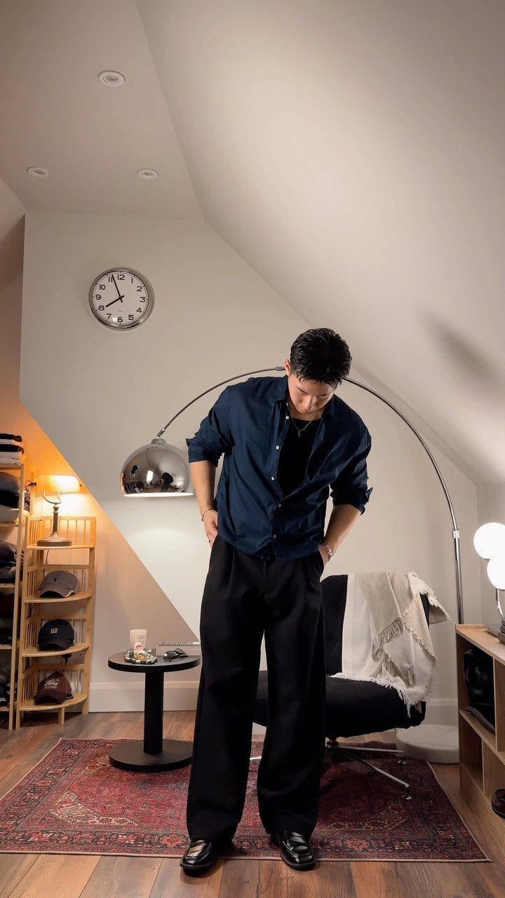 Man wearing a blue button-down shirt and wide black trousers in a modern room