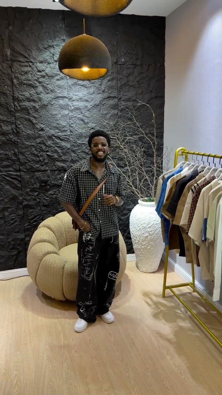 Man wearing a checkered shirt and patterned black pants in a modern room.