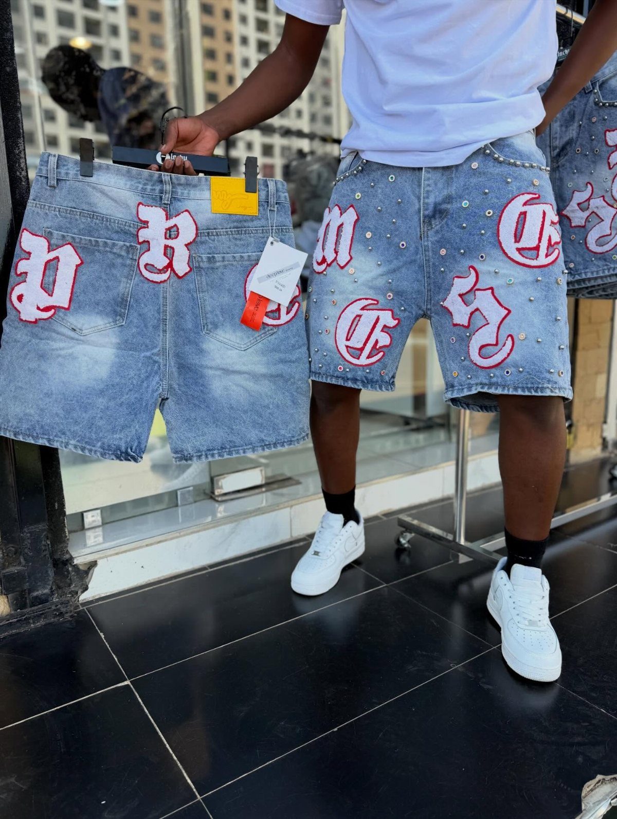 Light wash denim shorts with red and white cross patches and silver studs.