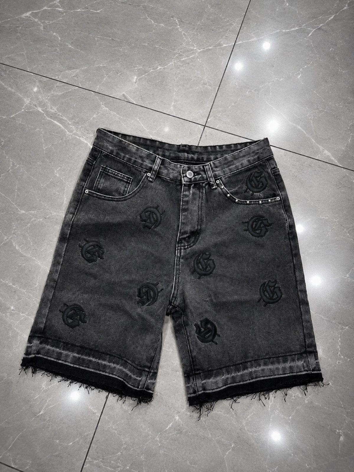 Dark grey denim shorts with black gothic embroidery on a marbled floor
