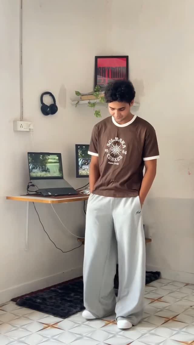 Young man wearing a brown graphic t-shirt and oversized grey sweatpants in a room.
