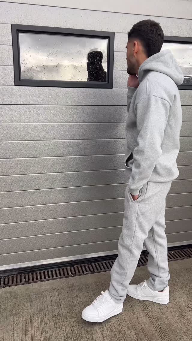 Man wearing a light grey hoodie and sweatpants with white sneakers.