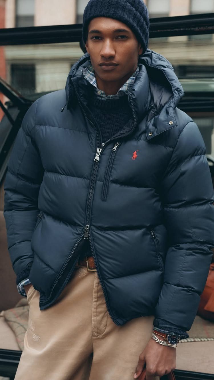 Man wearing a navy puffer jacket, dark beanie, and tan chinos in a city.