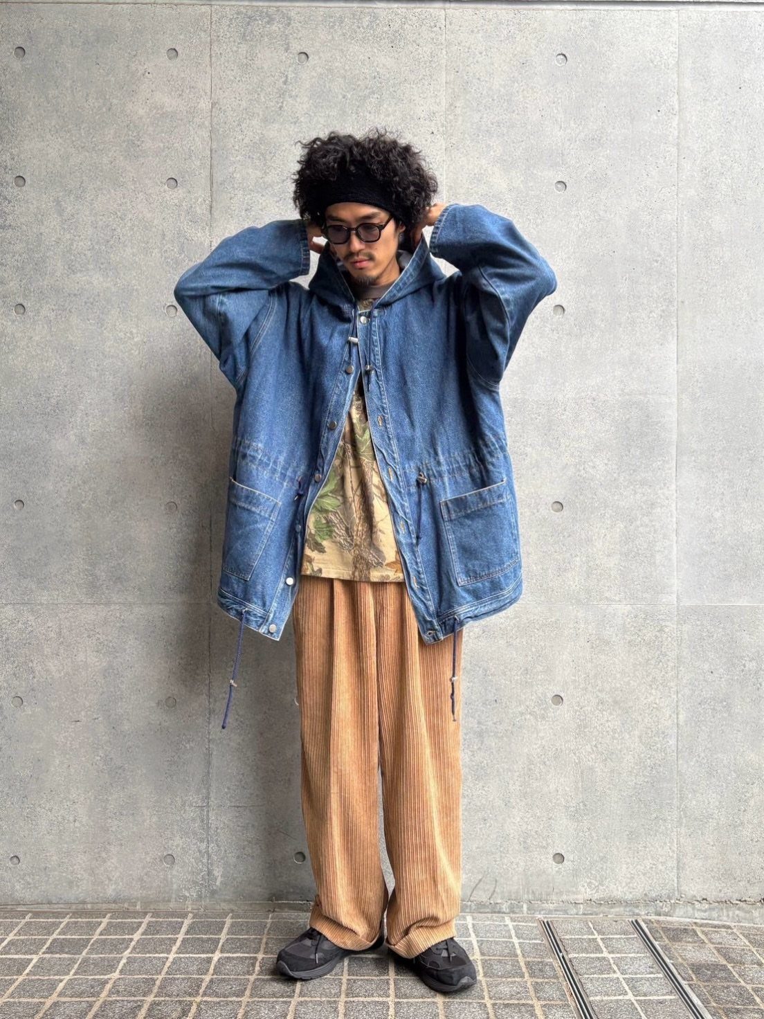 Man wearing an oversized blue denim jacket and wide-leg tan corduroy pants.