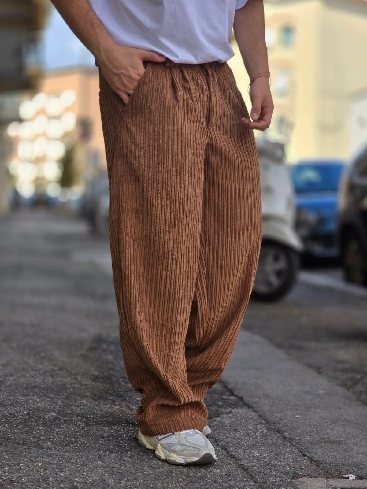 Man wearing loose brown corduroy pants and white sneakers on a city street