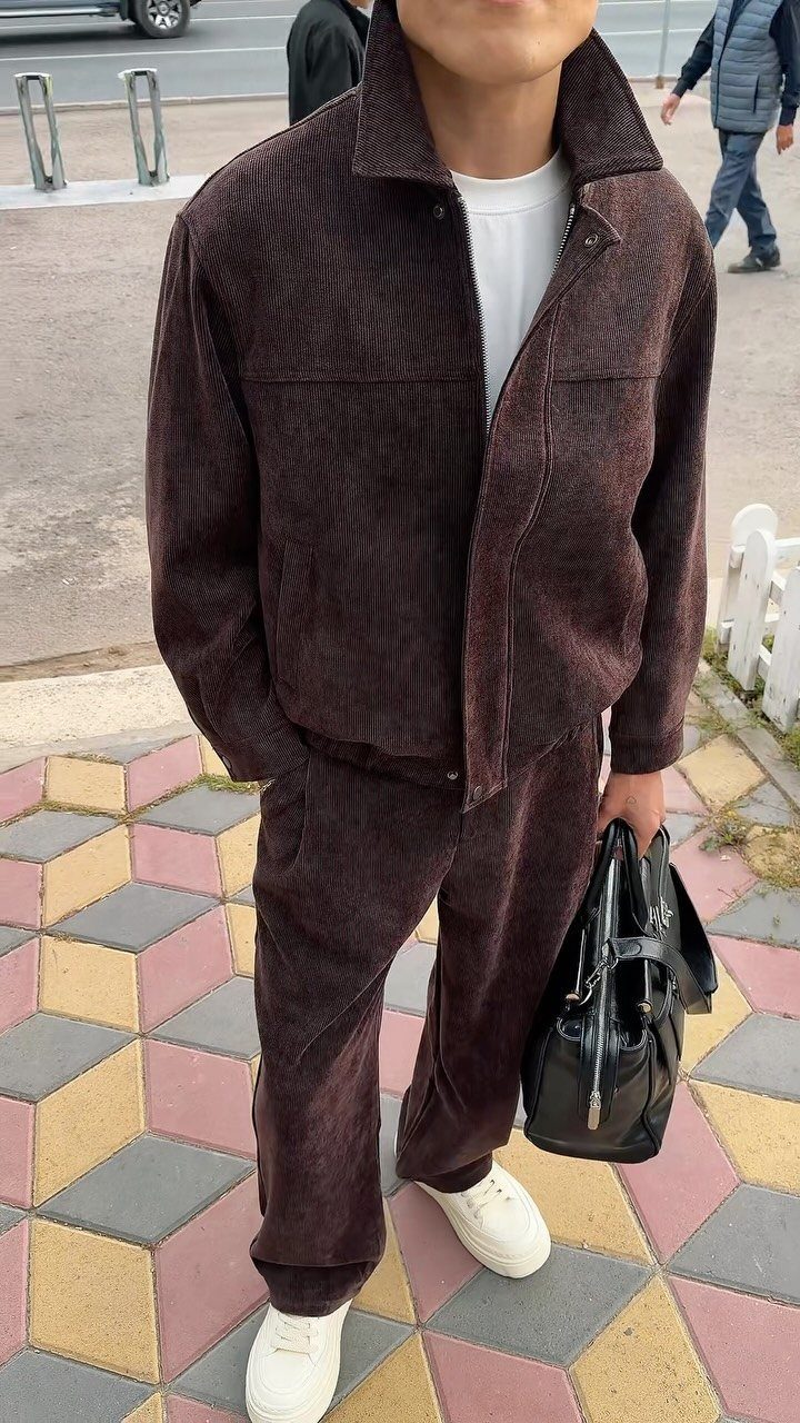 Man wearing a dark brown corduroy suit set with white sneakers and black bag.