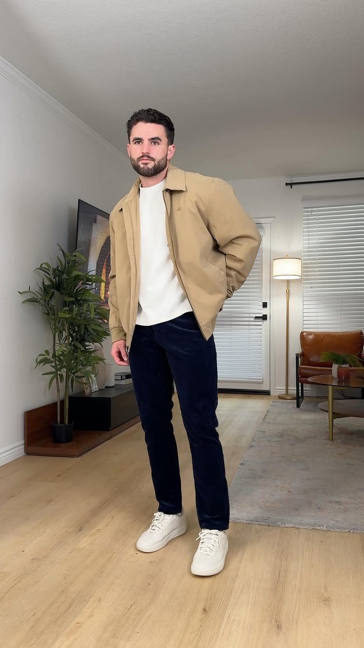 Man wearing navy blue corduroy pants, white t-shirt, tan jacket, and white sneakers.