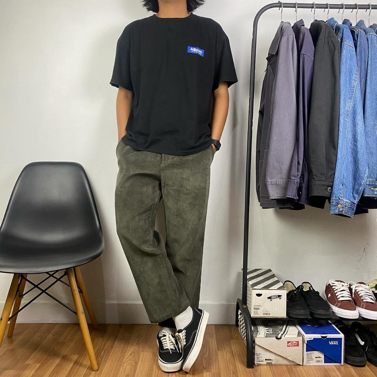 Person wearing olive green corduroy pants, black t-shirt, and black sneakers indoors.
