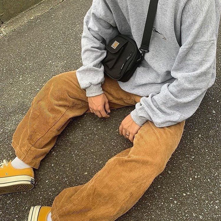 Person wearing brown corduroy pants, grey sweatshirt, and yellow sneakers sitting on pavement.