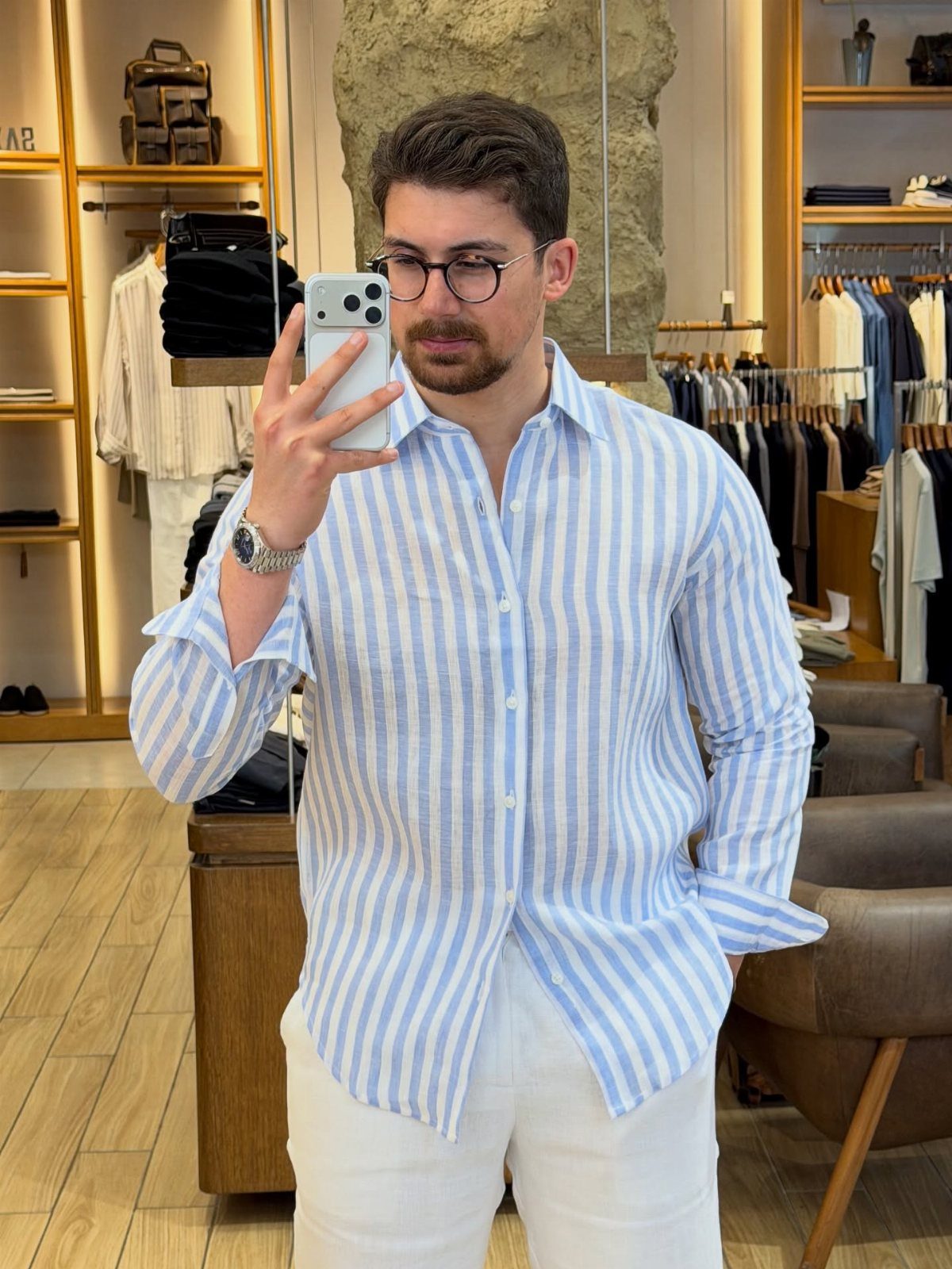 Man wearing a blue and white striped button-down shirt and white trousers.