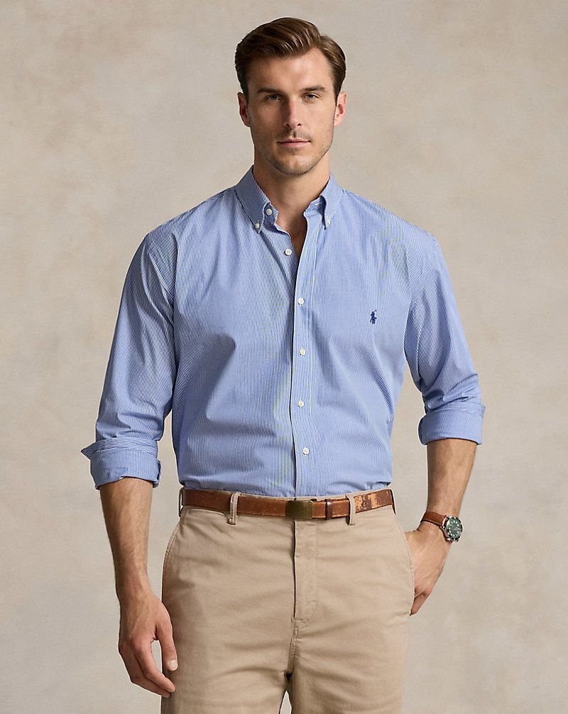 Man wearing a light blue button-down shirt tucked into khaki trousers with brown belt