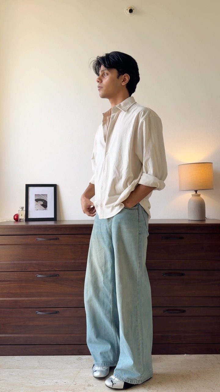 Man wearing an oversized white button-down shirt and wide-leg light blue jeans indoors.