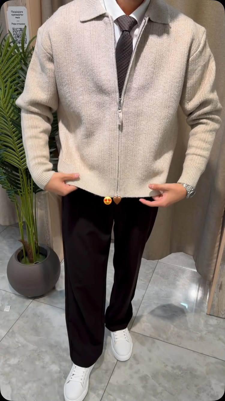 Man wearing a beige cropped zip-up knit jacket with black trousers and white sneakers.