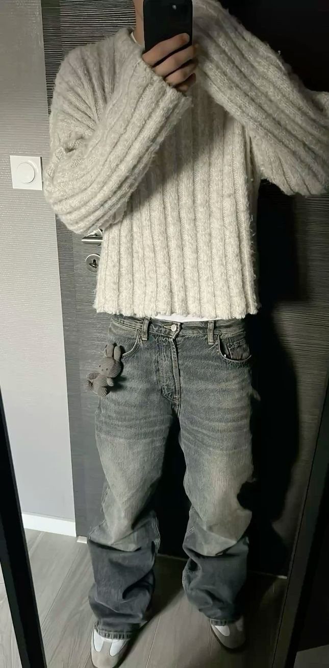 Person wearing a white cable-knit cropped sweater and baggy grey washed denim jeans.