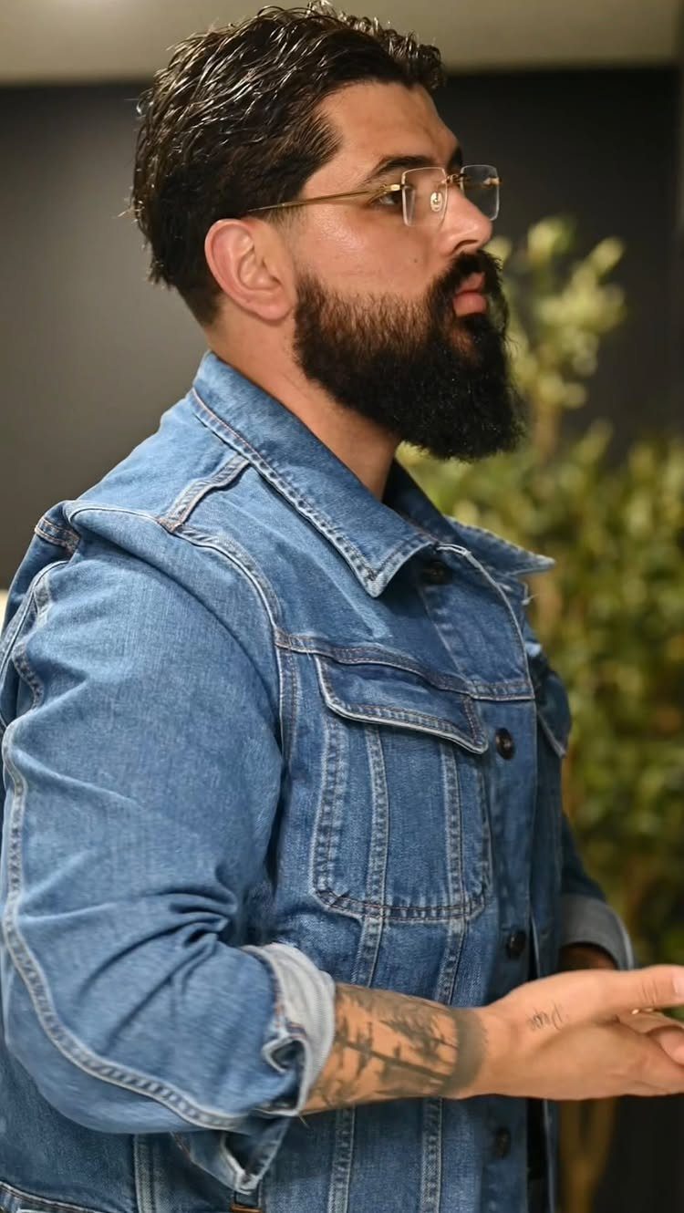 Man with beard and glasses wearing a blue denim jacket in profile