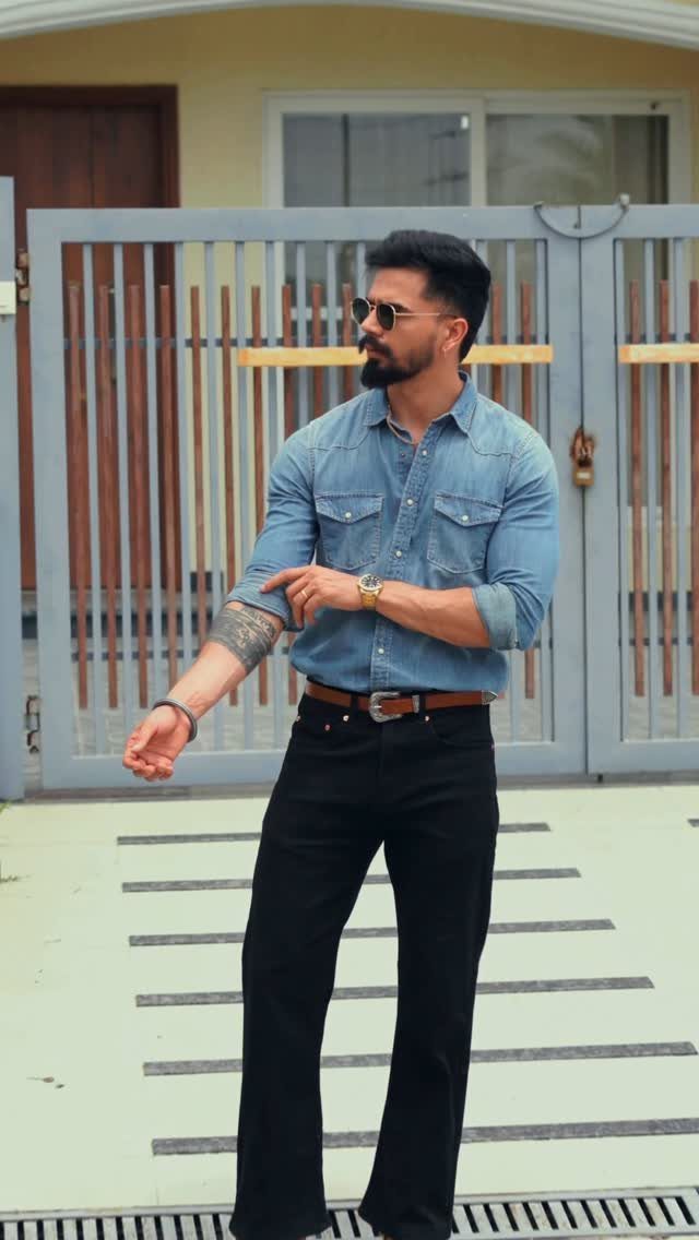 Man wearing a light blue denim shirt paired with black jeans and sunglasses.