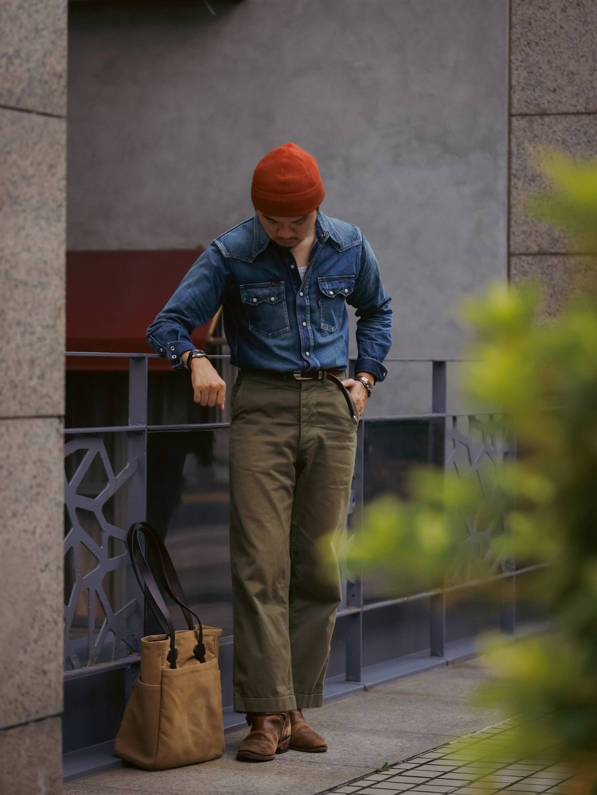 Man in blue denim shirt and olive green chinos wearing a red beanie.
