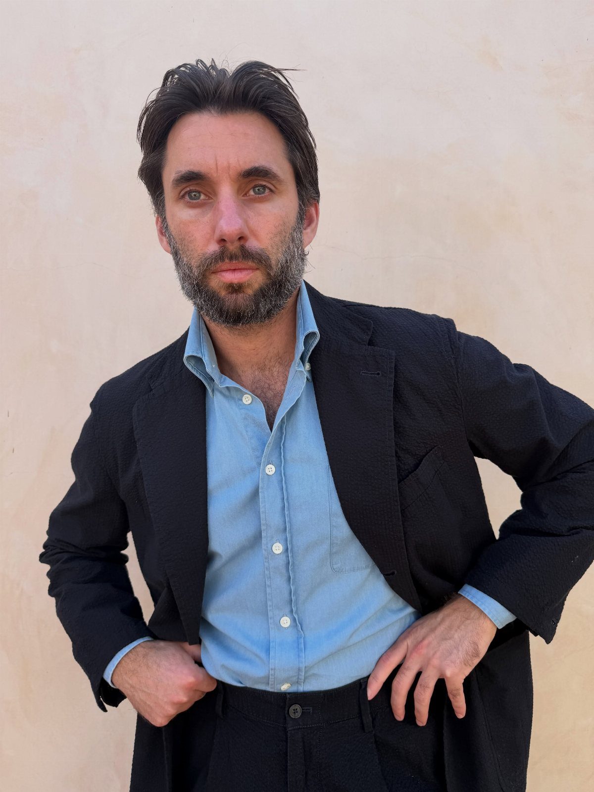 Man wearing a light blue denim shirt under a black blazer and trousers.