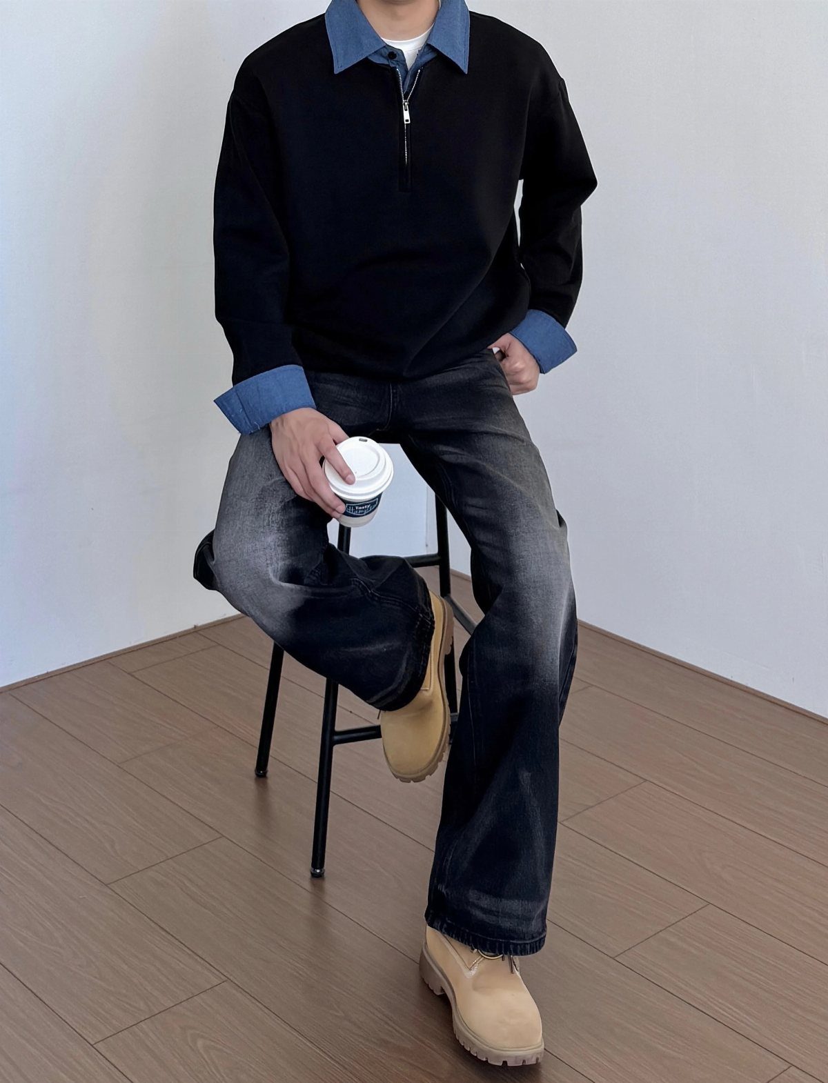 Person wearing a black sweater over a blue denim shirt and grey jeans.