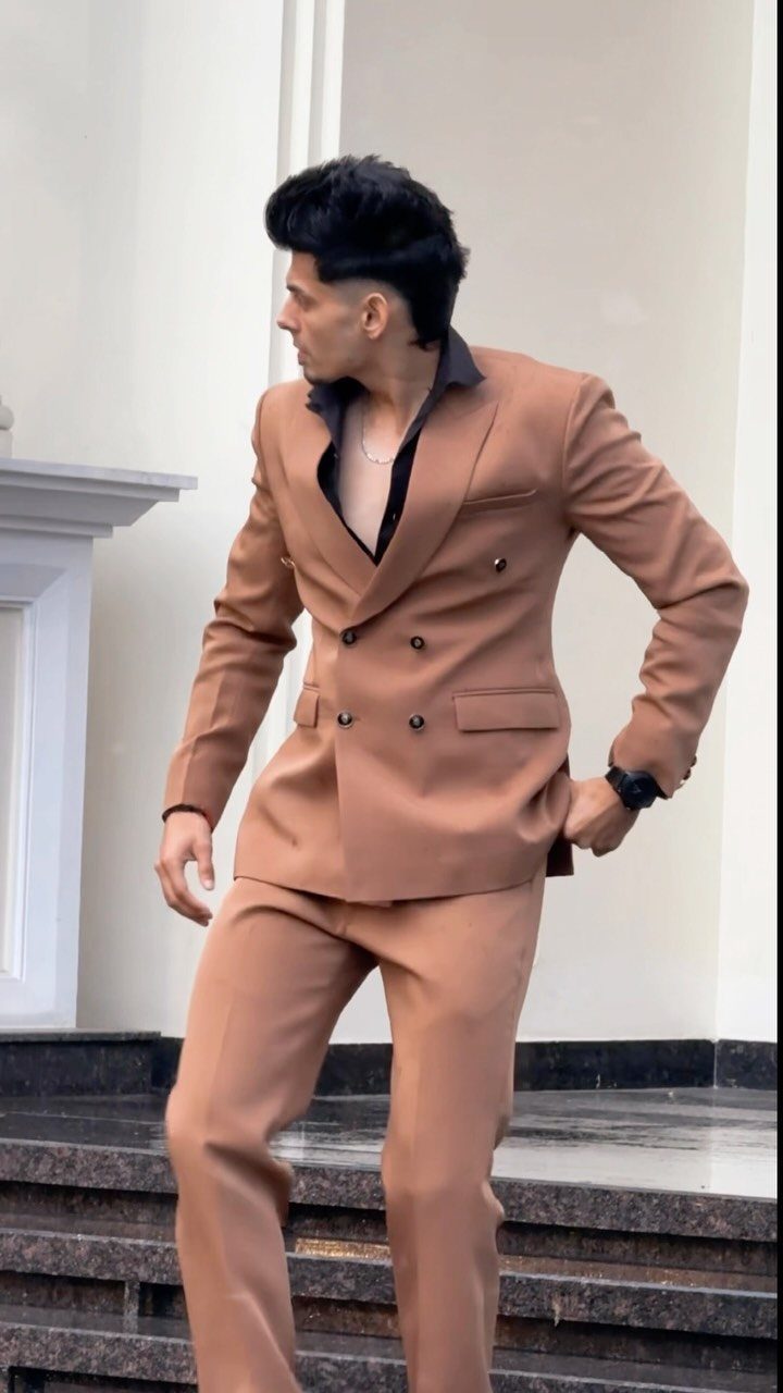 Man in a double-breasted brown suit and dark shirt standing on stone steps.