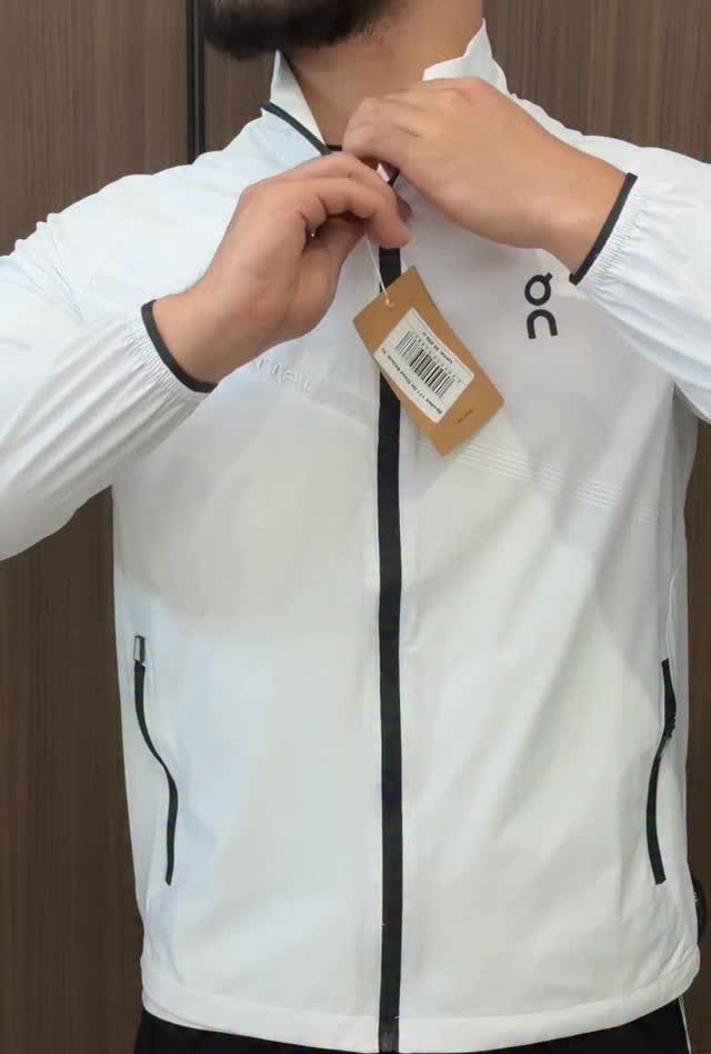Man wearing a white athletic zip-up jacket with black trim and a price tag.