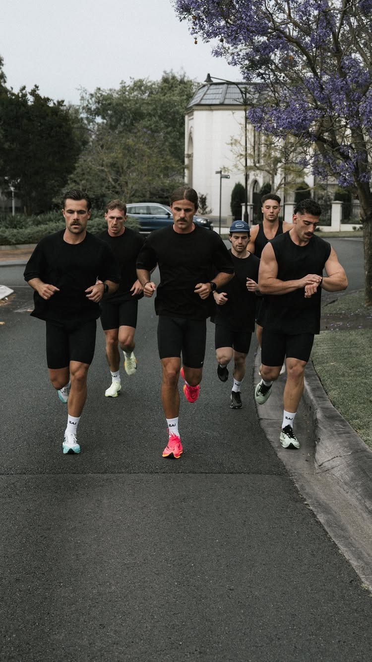 Five men in black athletic wear running together on a paved outdoor road.