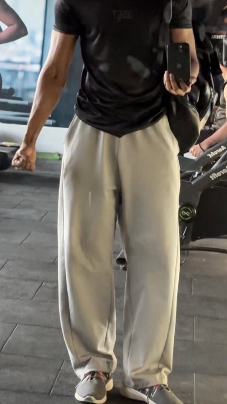 Man wearing a black t-shirt and loose grey sweatpants in a gym setting.