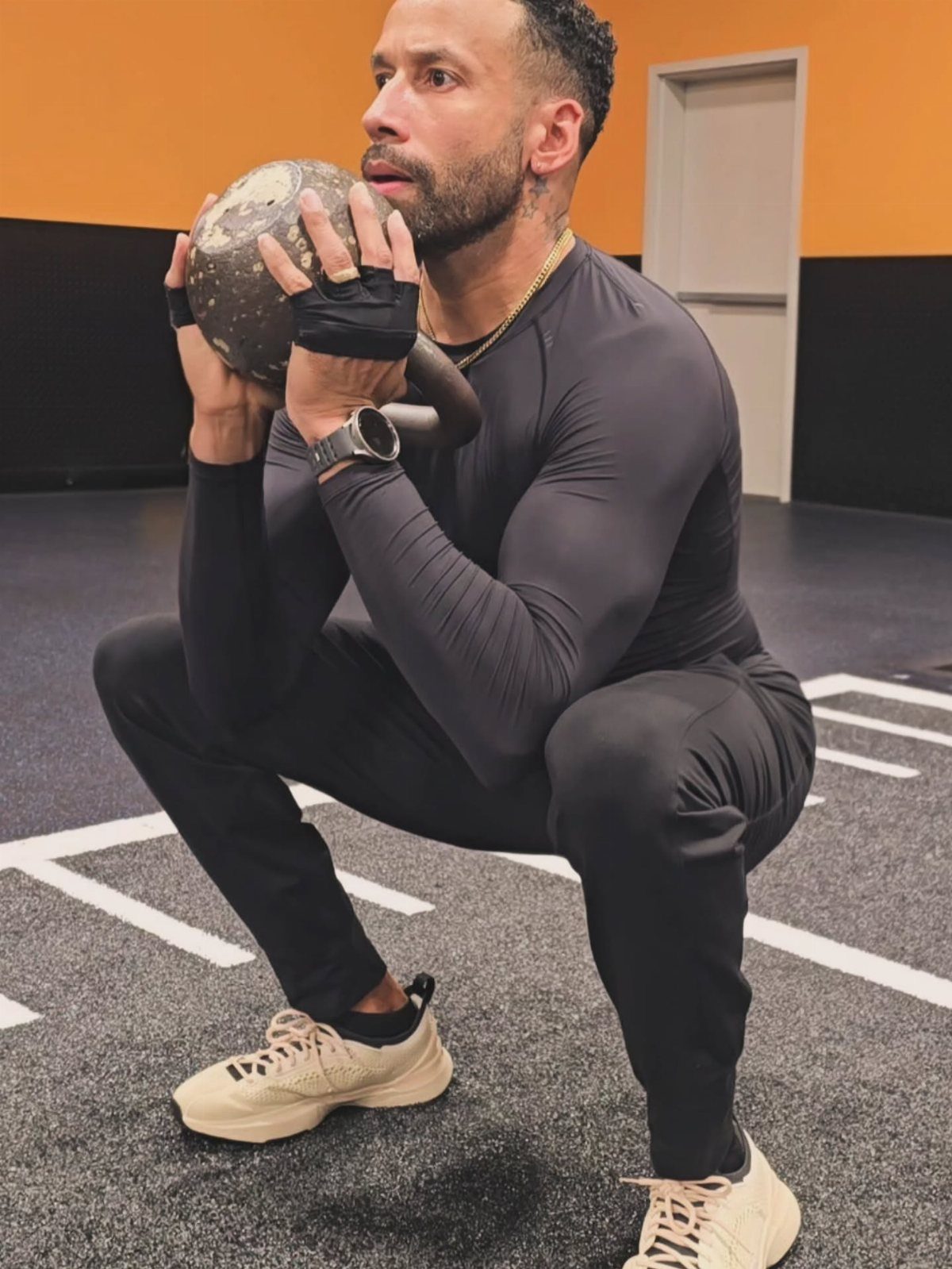 Man in tight black athletic wear holding a medicine ball in a gym