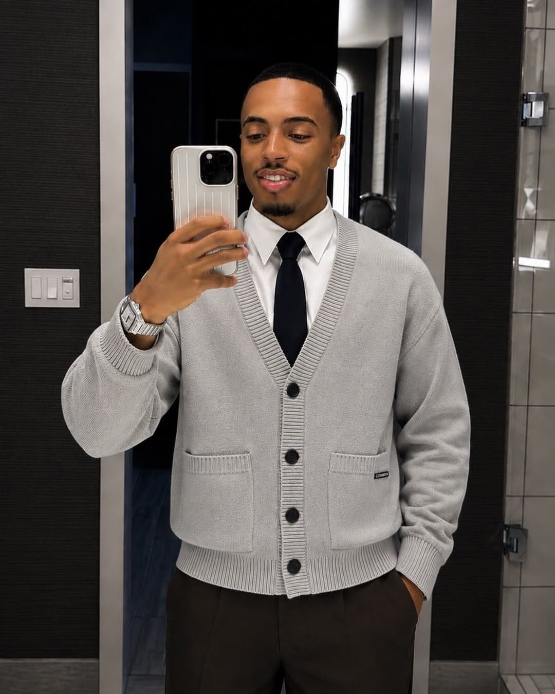 Man wearing a gray cardigan over a white collared shirt and dark tie.