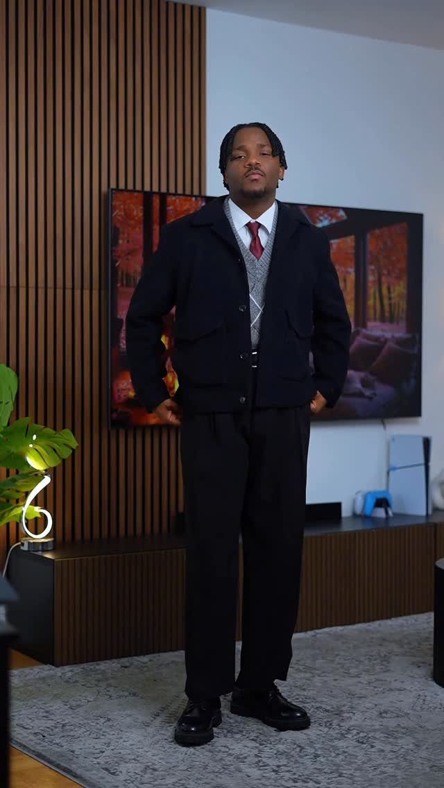 Man wearing a gray cardigan under a navy jacket with black trousers and tie.