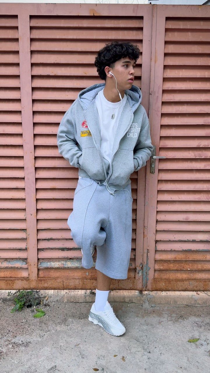 Young man wearing a grey hoodie and grey shorts standing by a door.