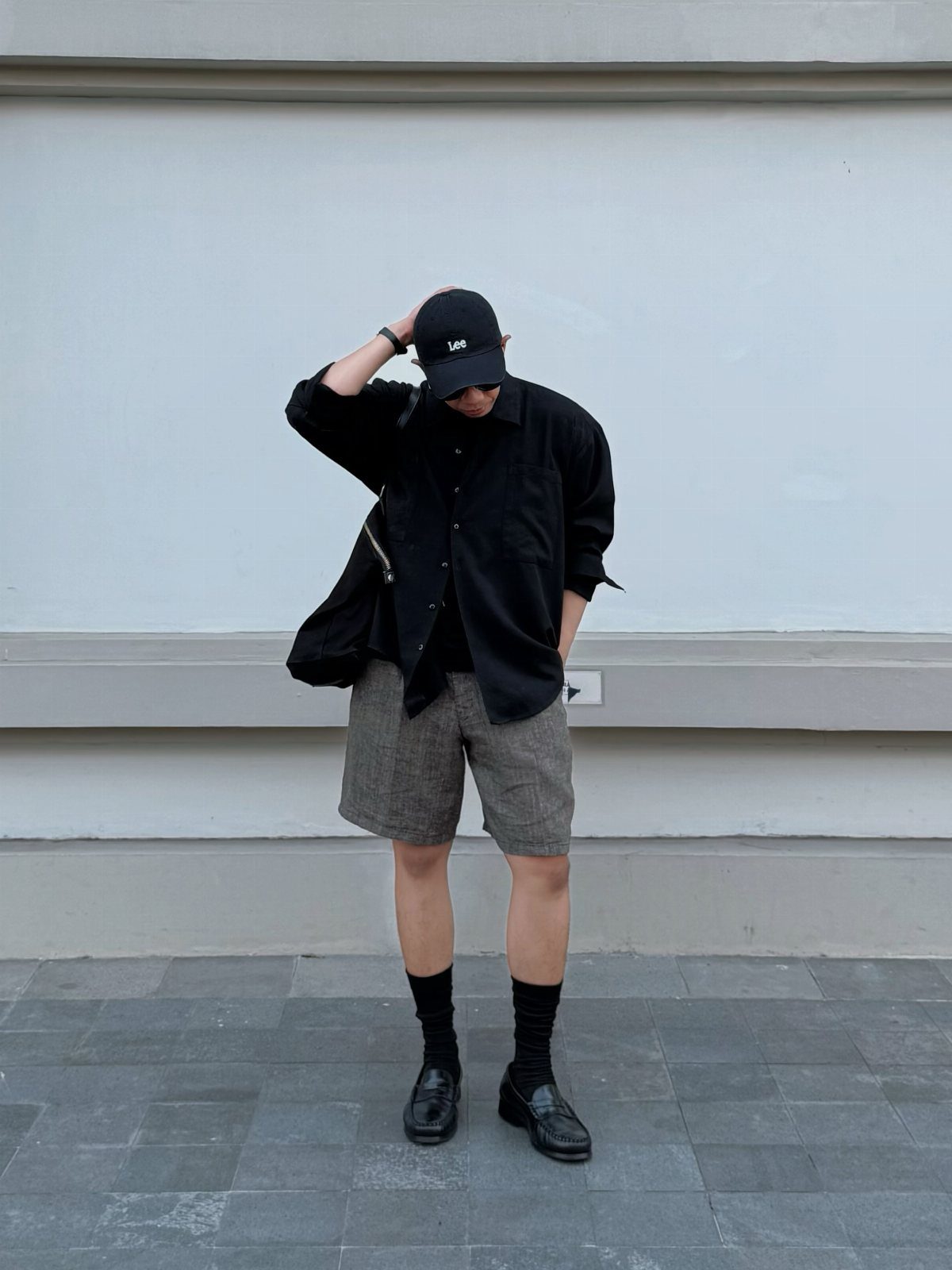 Person wearing black shirt, grey shorts, and black leather loafers against white wall