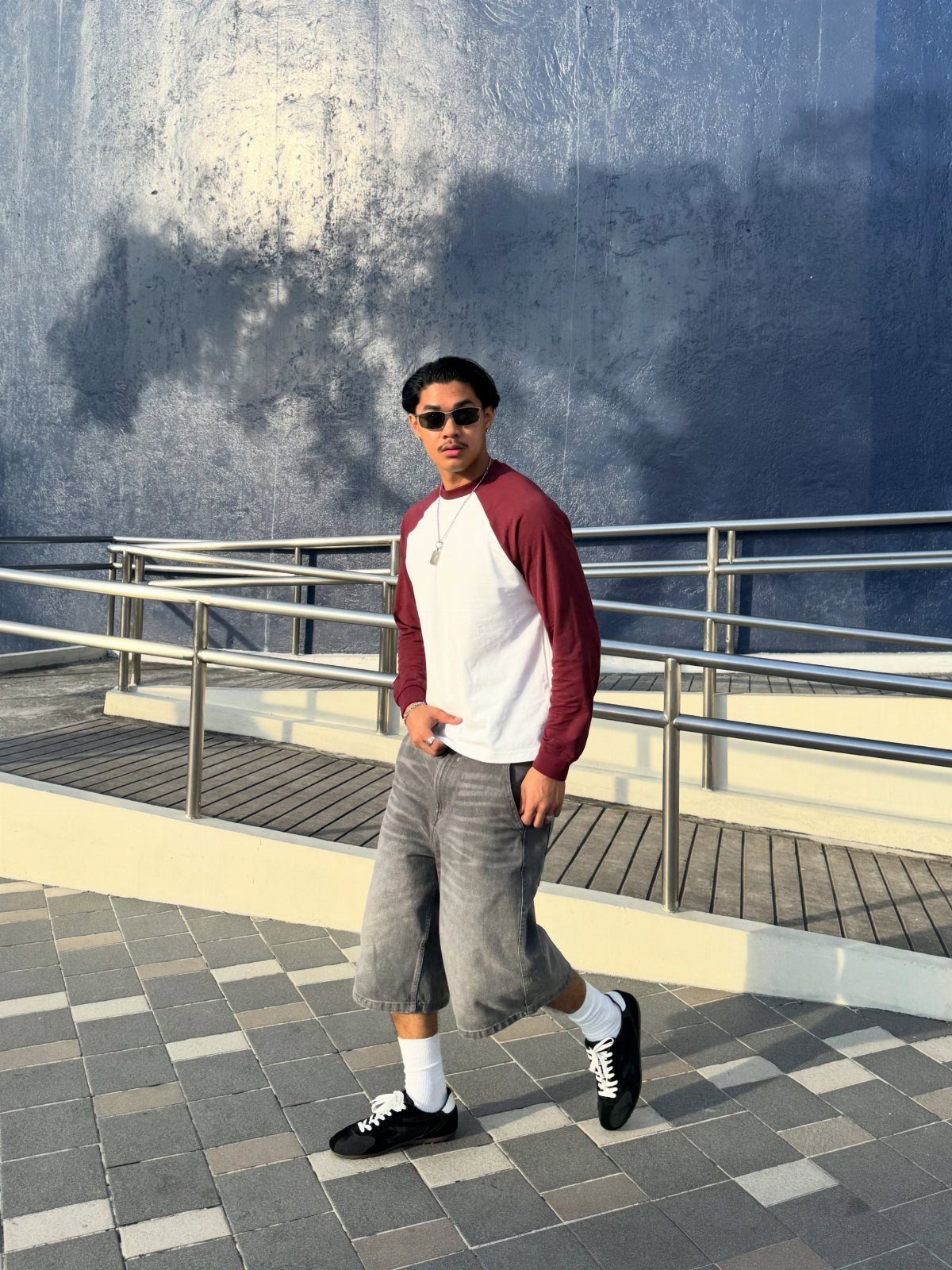 Man wearing a white and maroon raglan shirt with grey shorts and sneakers.
