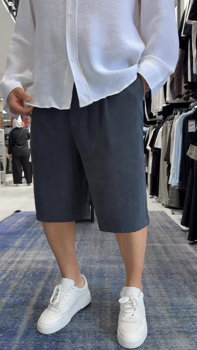 Person wearing a white shirt, dark grey shorts, and white sneakers in store.