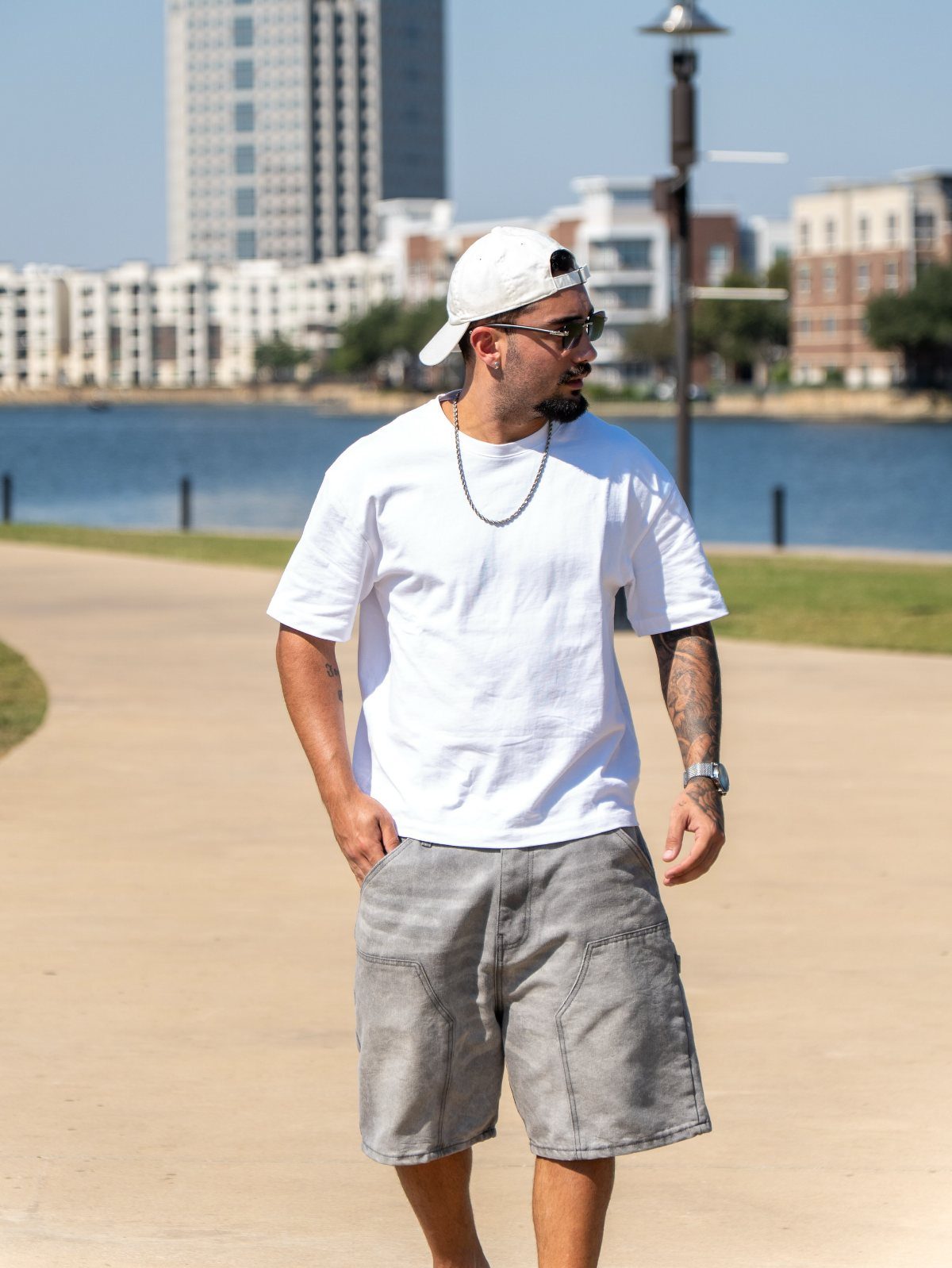 Man wearing a white t-shirt and grey shorts standing by a waterfront.