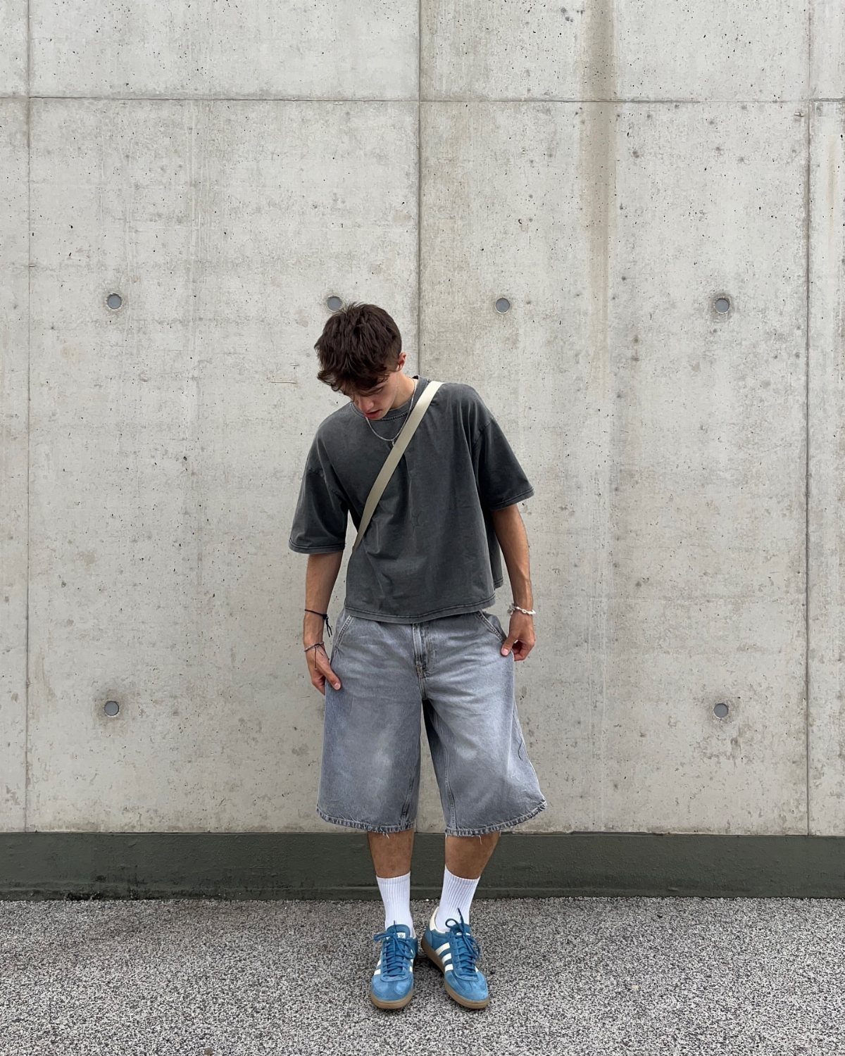Person wearing dark grey t-shirt and wide grey shorts with blue sneakers.